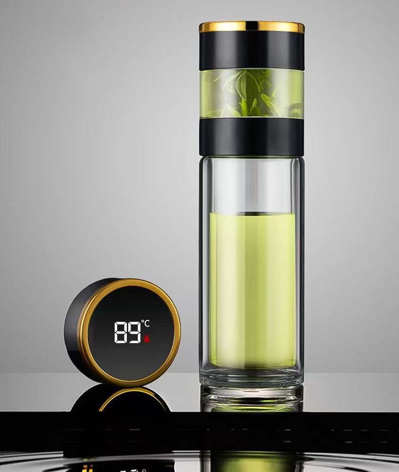 The Smart water boatel, featuring a black and gold lid and filled with light green liquid, stands beside a digital thermometer showing 89°C on a reflective surface against a gray background—ideal for hydration tracking.